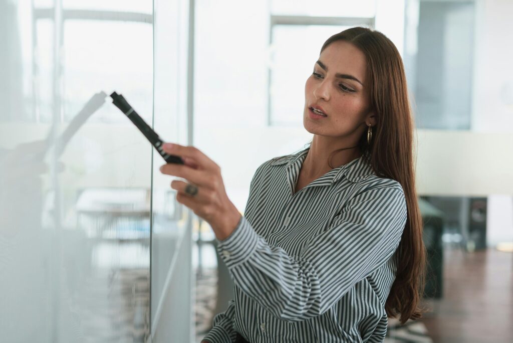 pexels photo 10041253 10041253 A focused businesswoman writing on a whiteboard during a presentation in a modern office.