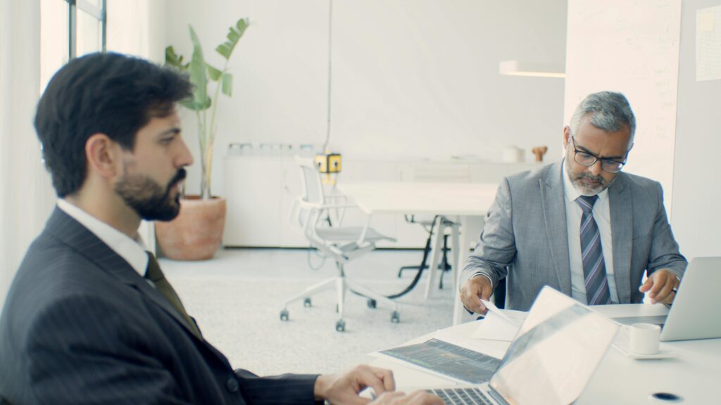 pexels photo 8463139 8463139 Two businessmen in formal suits working on laptops in a modern office setting.